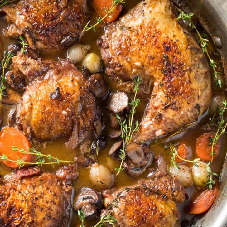 braised chicken with wine, bacon, mushrooms and onions in skillet