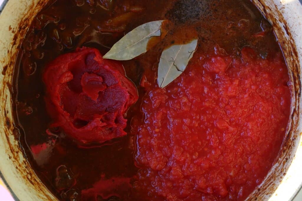 adding tomatoes and bay leaves to pot